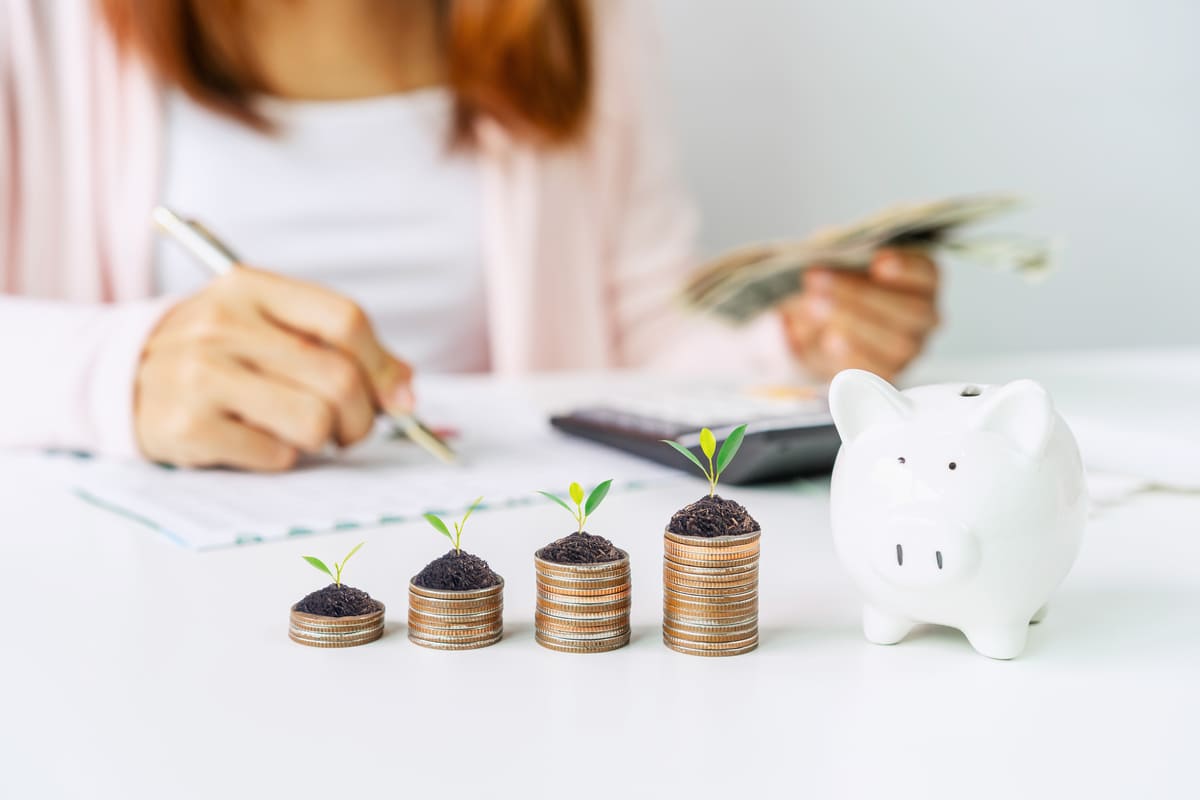 Stacked coins next to a piggy bank and a woman looking at charts
